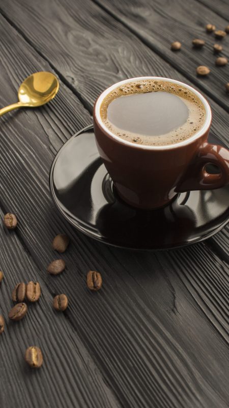 Black  coffee in the  brown ceramic cup on the black wooden background. Copy space. Vertical location.